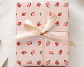 May include: A wrapped gift with pink wrapping paper featuring a pattern of red strawberries with green leaves. A cream-colored ribbon is tied around the gift in a bow.