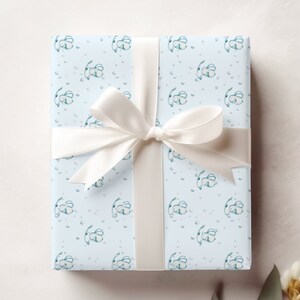 May include: A light blue gift box with a white ribbon and a pattern of small blue flowers. The box is wrapped in a light blue paper with a white ribbon tied in a bow.