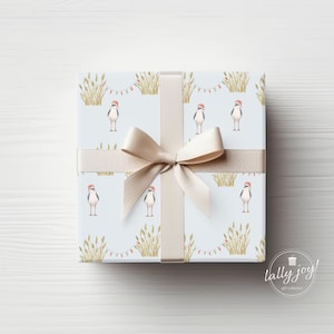 May include: A blue and white gift wrap with a pattern of birds wearing Santa hats and green grass. The gift is wrapped with a beige ribbon and bow. The text "lally joy! gift collection" is printed in the bottom right corner.