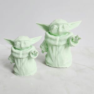 Pu&ograve; includere: Due sculture geometriche verde chiaro di un personaggio con grandi orecchie e un mantello con cappuccio. Le sculture sono di diverse dimensioni, una leggermente pi&ugrave; piccola dell'altra. Le figure hanno un design poligonale.