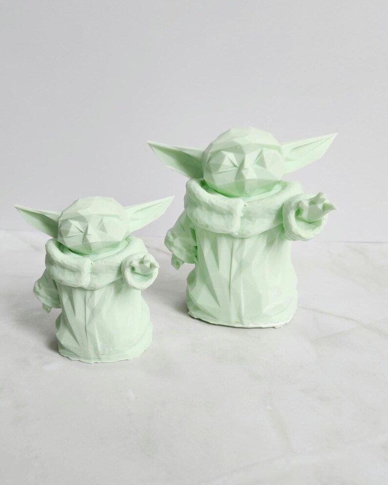 Pu&ograve; includere: Due sculture geometriche verde chiaro di un personaggio con grandi orecchie e un mantello con cappuccio. Le sculture sono di diverse dimensioni, una leggermente pi&ugrave; piccola dell'altra. Le figure hanno un design poligonale.