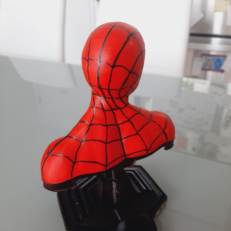 May include: A red and black Spider-Man bust figurine. The bust features a red head and shoulders with a black web pattern. The base is black. The figurine is a collectible item.