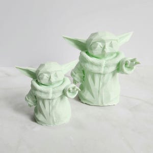 Pu&ograve; includere: Due sculture geometriche verde chiaro di un personaggio con grandi orecchie e un mantello con cappuccio. Le sculture sono in posizione eretta, una leggermente pi&ugrave; piccola dell'altra. Le figure hanno un design poligonale.