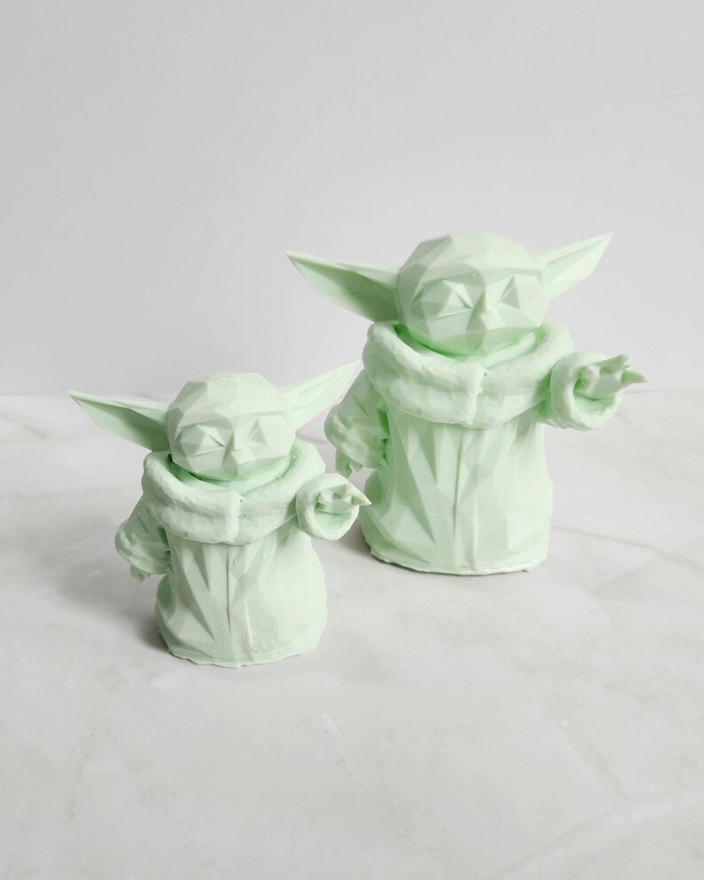 Pu&ograve; includere: Due sculture geometriche verde chiaro di un personaggio con grandi orecchie e un mantello con cappuccio. Le sculture sono in posizione eretta, una leggermente pi&ugrave; piccola dell'altra. Le figure hanno un design poligonale.