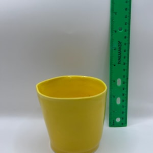 May include: A bright yellow ceramic cup with a slightly irregular, organic rim. A green Trailmaker ruler is positioned vertically next to the cup, showing the cup stands at a height of approximately 3.5 inches.