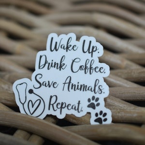 May include: A set of three ceramic mugs with a speckled, cream-colored glaze. Each mug features a different hand-painted design: a blue and green leaf, a yellow and orange flower, and a red berry sprig. The mugs have a simple, rounded shape.