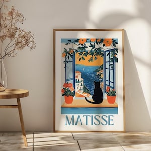 以下が含まれることがあります： 海岸の風景を眺める開いた窓から外を眺める黒猫のシルエットが描かれた、額入りのアートプリントです。「MATISSE」の文字が薄い青色でプリントされています。オレンジ色の花と緑が窓を縁取っています。