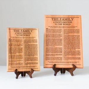 Puede incluir: Dos placas de madera con el texto "THE FAMILY A PROCLAMATION TO THE WORLD" se muestran. Las placas están sobre pequeños soportes de madera. El texto está impreso en negro sobre la madera de color marrón claro. Las placas son de diferentes tamaños.