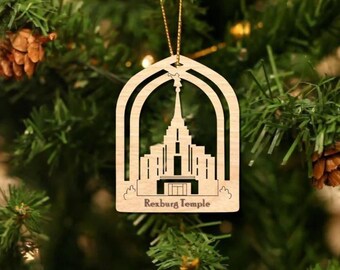 Puede incluir: Adorno navideño de madera con un diseño recortado del Templo de Rexburg, Idaho. El adorno es marrón y tiene una cuerda dorada para colgar.