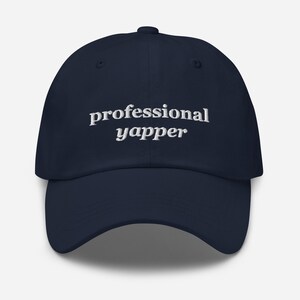 May include: A navy blue baseball cap with white embroidered text that reads "professional yapper".