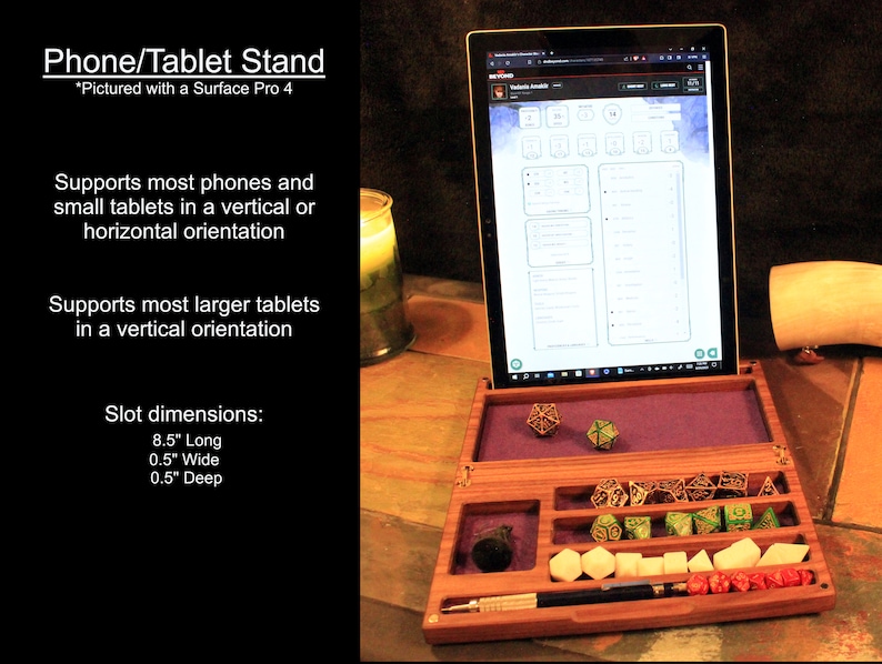 May include: A wooden phone and tablet stand with a purple felt lining. The stand has a slot for holding a tablet or phone in a vertical orientation. The stand also has a compartment for dice and other gaming accessories. The stand is pictured with a Surface Pro 4 tablet.