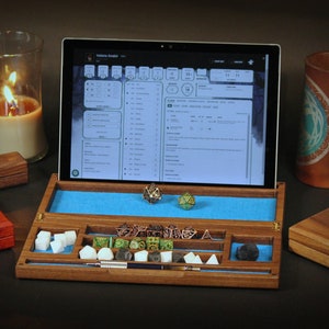 May include: A wooden box with a blue felt interior and compartments for dice and other gaming accessories. The box is open and contains a variety of dice, including a d20, a d12, a d10, a d8, a d6, and a d4. There is also a pen and a small metal container. A tablet computer is open to a character sheet for a role-playing game.