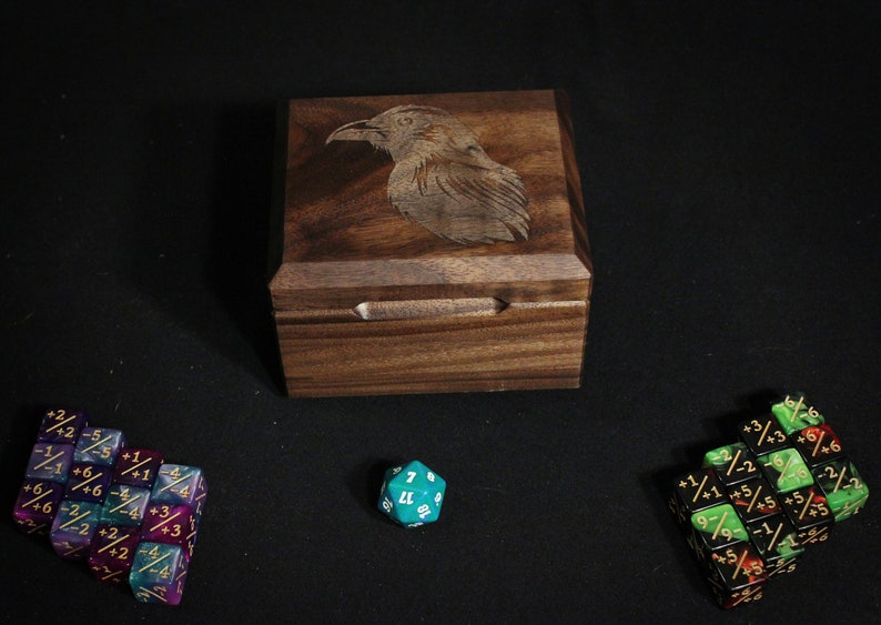 Walnut Deck Box with lid closed surrounded by counter dice, raven engraving on lid shown.