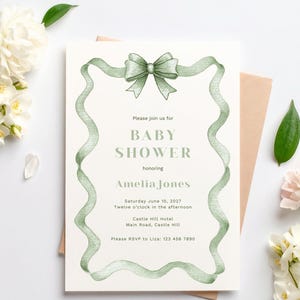 Puede incluir: Invitaci&oacute;n a un baby shower con un dise&ntilde;o de lazo y cinta verde. La invitaci&oacute;n incluye el texto "Baby Shower" y los detalles de la fiesta de Amelia Jones el 10 de junio de 2027, en el Hotel Castle Hill. Tambi&eacute;n se ven flores blancas y un sobre rosa.