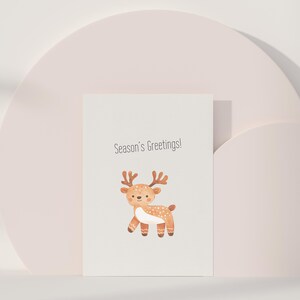 Puede incluir: Una tarjeta blanca con el texto "Season's Greetings!" y una ilustraci&oacute;n de dibujos animados de un reno marr&oacute;n con manchas blancas.