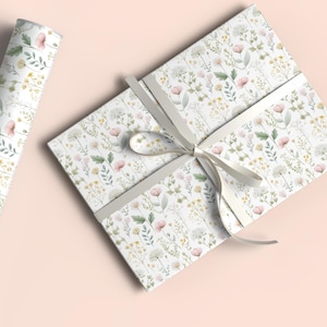 May include: A roll of floral wrapping paper and a wrapped gift box. The paper and box feature a delicate pattern of pink, yellow, and white wildflowers on a white background. A light gray ribbon is tied around the box.