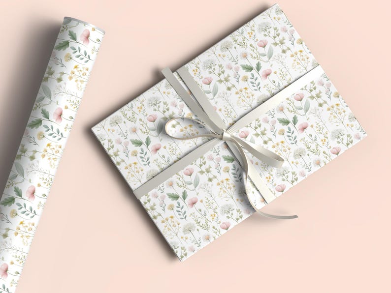 May include: A roll of floral wrapping paper and a wrapped gift box. The paper and box feature a delicate pattern of pink, yellow, and white wildflowers on a white background. A light gray ribbon is tied around the box.