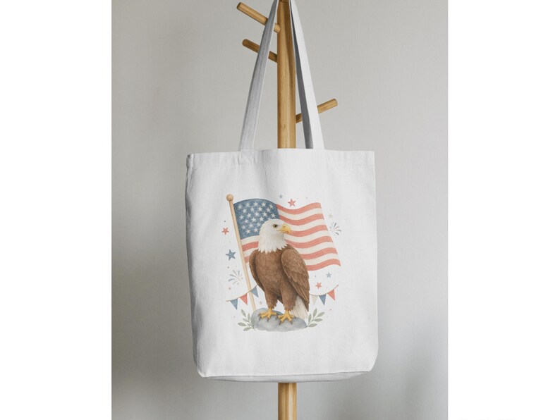 May include: White tote bag featuring a watercolor illustration of an American bald eagle standing before a waving American flag. The flag has red and white stripes and a blue field with white stars. The eagle is brown and white.