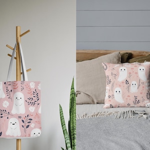Pu&ograve; includere: Una borsa tote rosa e un cuscino rosa con un motivo di fantasmi bianchi. I fantasmi hanno un design carino e cartonato. La borsa tote ha un manico bianco. Il cuscino &egrave; su un letto con una coperta grigia.