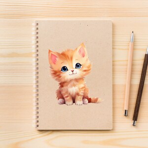 May include: A brown spiral bound notebook with a cute cartoon illustration of a ginger kitten with blue eyes. The notebook is on a light wood surface with two pens, one brown and one light wood.