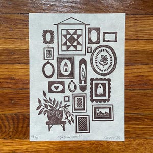 May include: A brown and white print of a gallery wall with various framed images, including a quilt pattern, a heart, a flower, and a ghost. A potted plant is at the bottom left. The text "gallerywall" is below the images, with "11/28" and "lam '25" at the bottom.