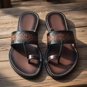 May include: A pair of brown leather sandals with a toe loop design. The sandals feature a dark brown strap with an embossed geometric pattern and a braided toe strap. The soles are a lighter brown with white stitching.