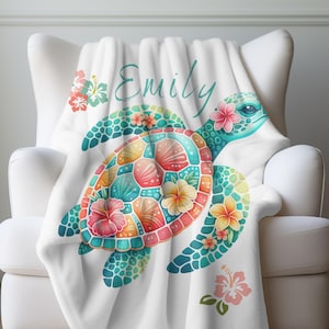 May include: White fleece throw blanket with a colorful sea turtle design and the name "Emily" printed on it. The turtle has a mosaic-like shell with flowers and leaves.