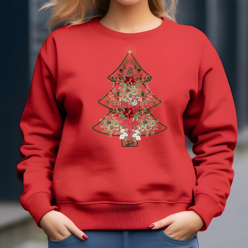 May include: Red sweatshirt featuring a Christmas tree design. The tree is outlined in green and filled with festive elements like pinecones, poinsettias, and berries. A gold star tops the tree, creating a holiday-themed apparel item.