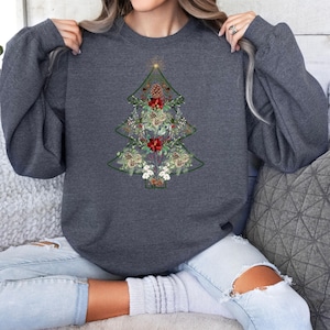 May include: A dark gray sweatshirt featuring a Christmas tree design. The tree is outlined in green and filled with floral and pinecone elements in shades of red, white, and beige. The sweatshirt has long sleeves.