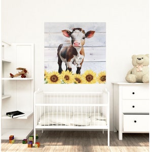 Puede incluir: Una pintura de acuarela de una vaca marr&oacute;n y blanca con la nariz rosa de pie frente a un fondo de tablones de madera. La vaca est&aacute; rodeada de girasoles amarillos.