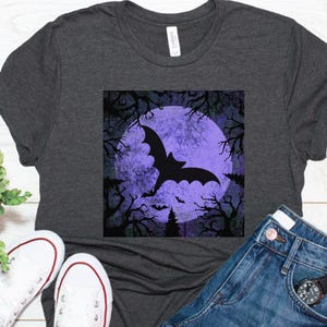 May include: A dark gray t-shirt with a purple and black graphic of a bat flying in front of a full moon. The graphic has a vintage, distressed look.