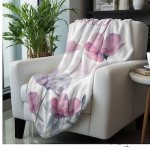 Puede incluir: Una manta blanca con un dise&ntilde;o floral de acuarela en tonos de rosa y morado. La manta presenta un patr&oacute;n floral con la palabra "pretty" impresa en ella.