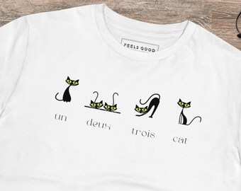 May include: White t-shirt featuring a black cat graphic and the text "un, deux, trois, cat". The shirt has a "Feels Good" tag on the collar.