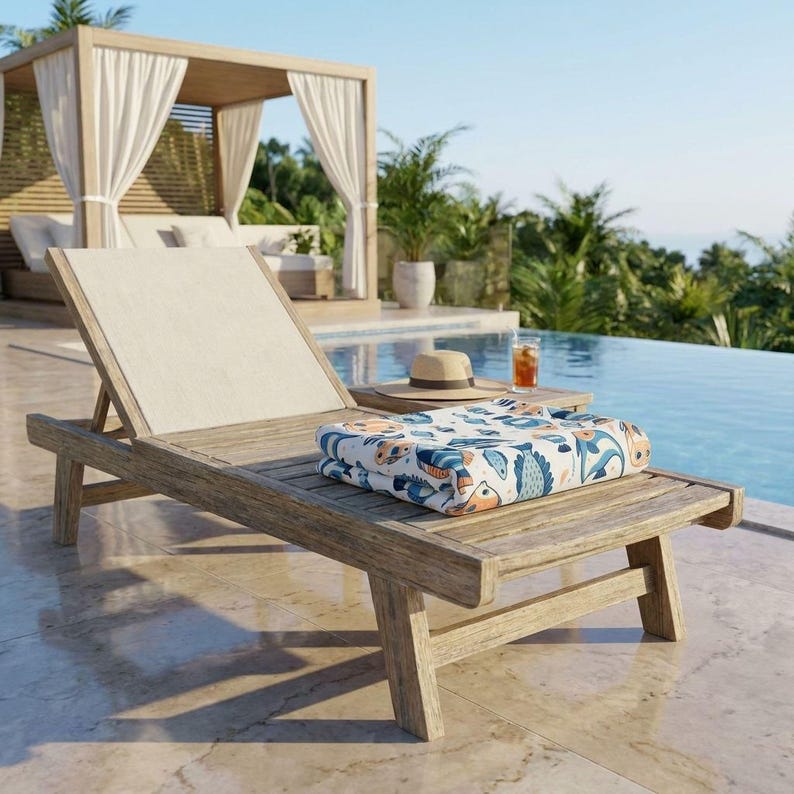 A wooden lounge chair with a colorful towel and a glass of orange juice sits on a tiled patio overlooking a pool, with a wooden pavilion and palm trees in the background.