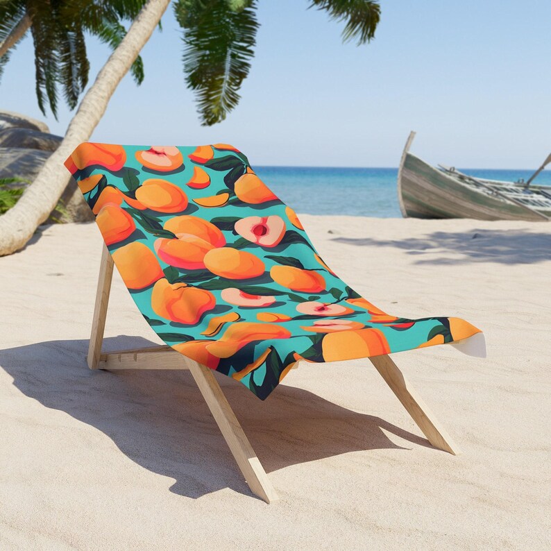 A colorful beach towel with an orange and green pattern is draped over a wooden chair on a sandy beach, with palm trees and a boat visible in the background.