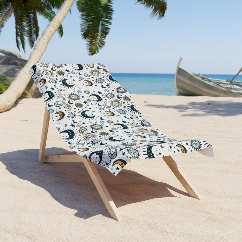 A beach chair with a patterned towel draped over it, situated on a sandy beach with palm trees and a boat visible in the background.