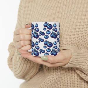 A person is holding a white mug with a blueberry pattern on it.
