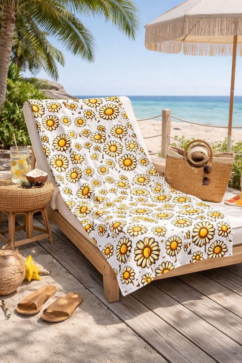 A comfortable lounge chair with a yellow and white floral patterned blanket, placed on a wooden deck overlooking a beach. The chair is accompanied by a straw umbrella, a woven basket, and a pair of sandals.