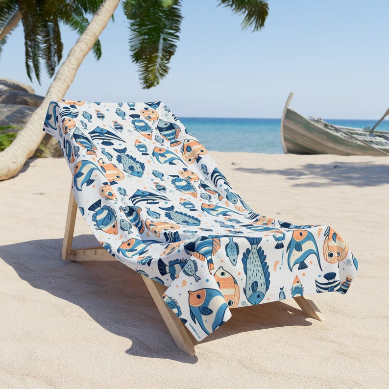A colorful beach towel with fish patterns is draped over a wooden chair on a sandy beach, with palm trees and a boat visible in the background.