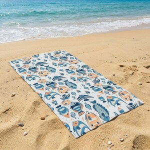 A colorful beach towel with a fish pattern lies on the sandy beach, with the ocean visible in the background.