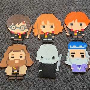 Puede incluir: Seis personajes de pixel art de la serie Harry Potter. Los personajes son Harry Potter, Ron Weasley, Hermione Granger, Severus Snape, Albus Dumbledore y Draco Malfoy. Cada personaje está hecho de pequeñas cuentas cuadradas de varios colores.