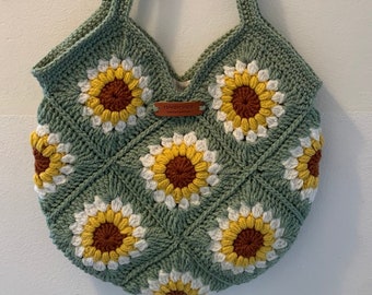 May include: A green crocheted tote bag with sunflower designs. The bag has a brown leather tag with the text "Handmade" on it.