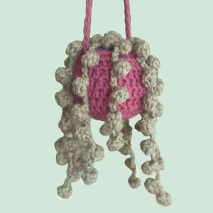 May include: A pink crocheted ball with beige crocheted tentacles hanging from it. The ball is attached to a beige string.