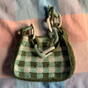 May include: A green and white checkered crocheted bag with a thick crocheted strap.