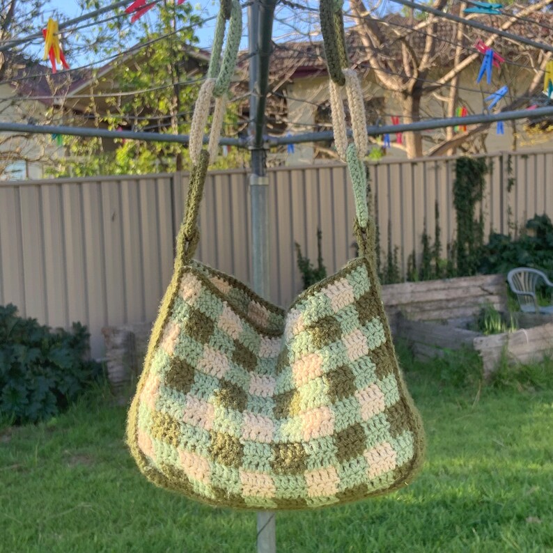 May include: A green and cream checkered crocheted tote bag hanging on a clothesline.