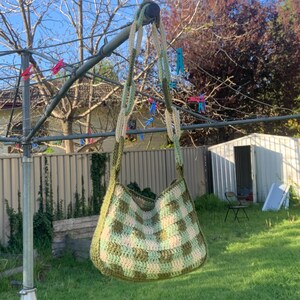 May include: A green and white crocheted tote bag hanging on a clothesline. The bag has a checkered pattern and a long strap.