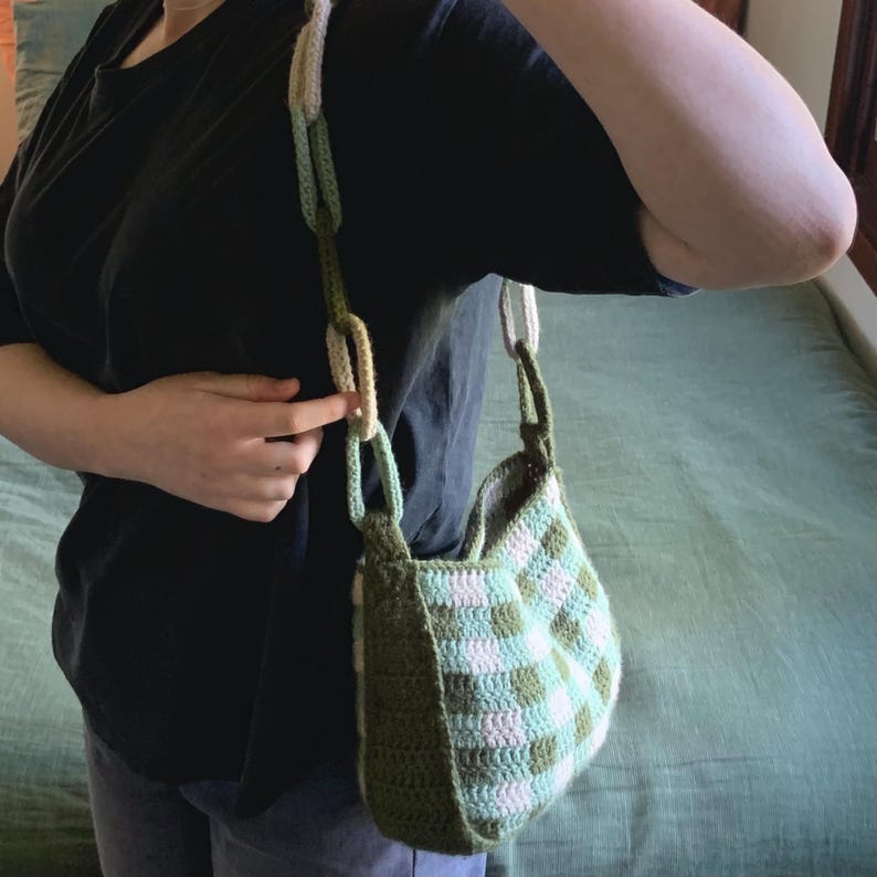 May include: A green and white crocheted shoulder bag with a thick crocheted strap. The bag has a checkered pattern.