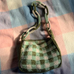May include: A green and white crocheted checkered shoulder bag with a long green and white crocheted strap.