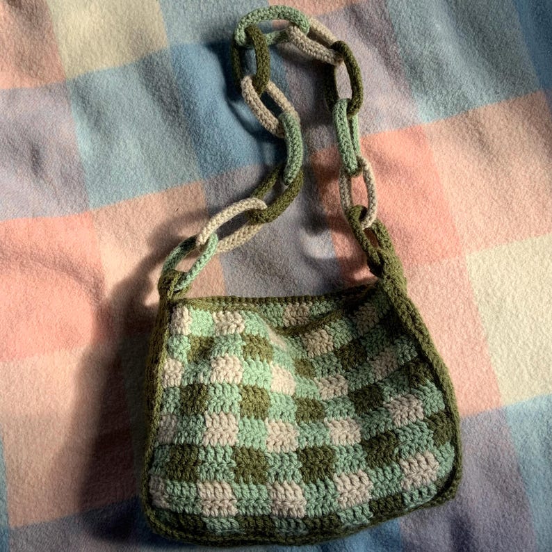 May include: A green and white crocheted checkered shoulder bag with a long green and white crocheted strap.