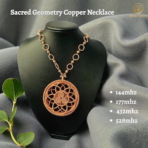 May include: A copper necklace with a circular pendant featuring a sacred geometry design. The necklace is displayed on a black bust against a grey backdrop. The text "Sacred Geometry Copper Necklace" is at the top.